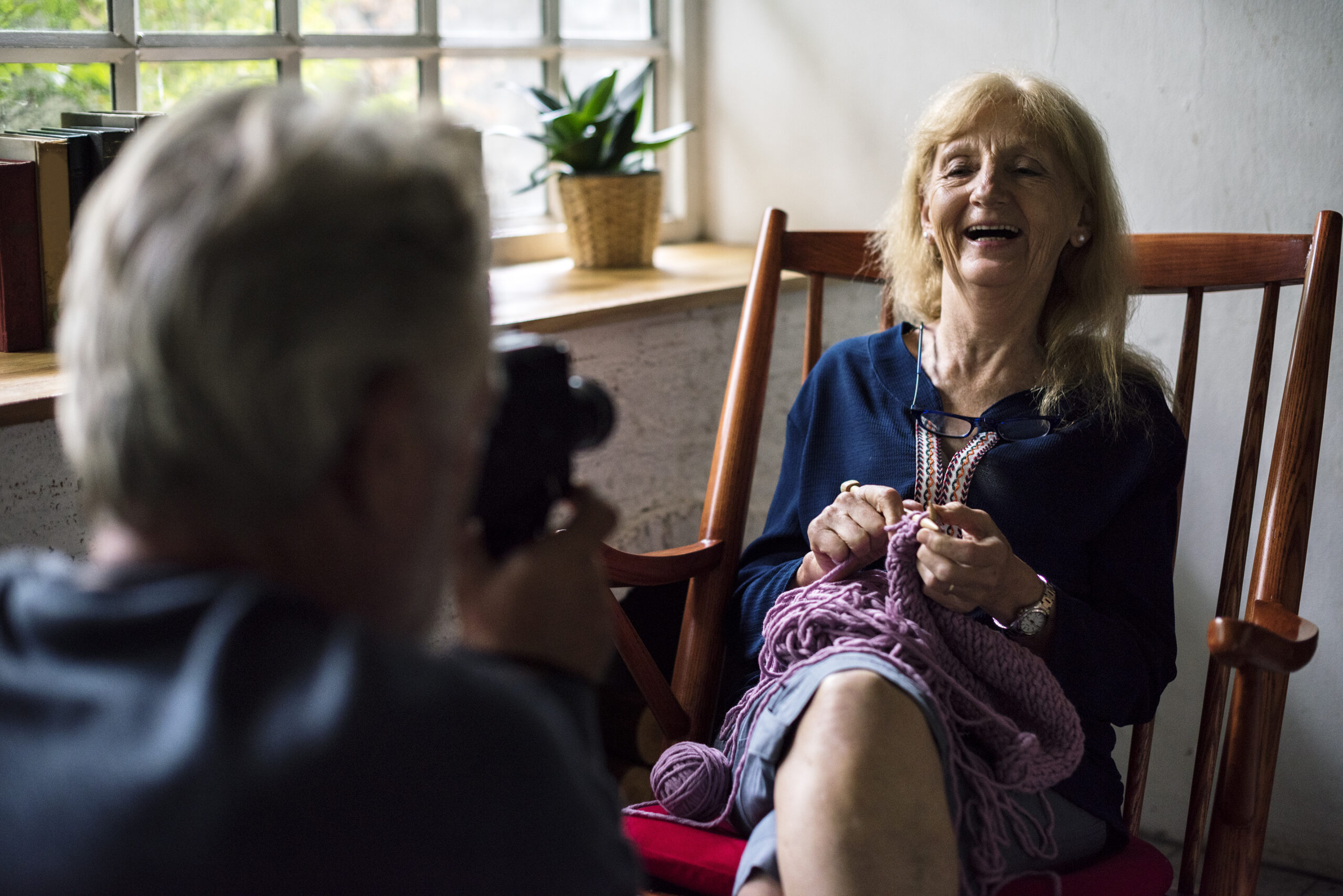 happy senior woman being videotaped for an interview while knitting