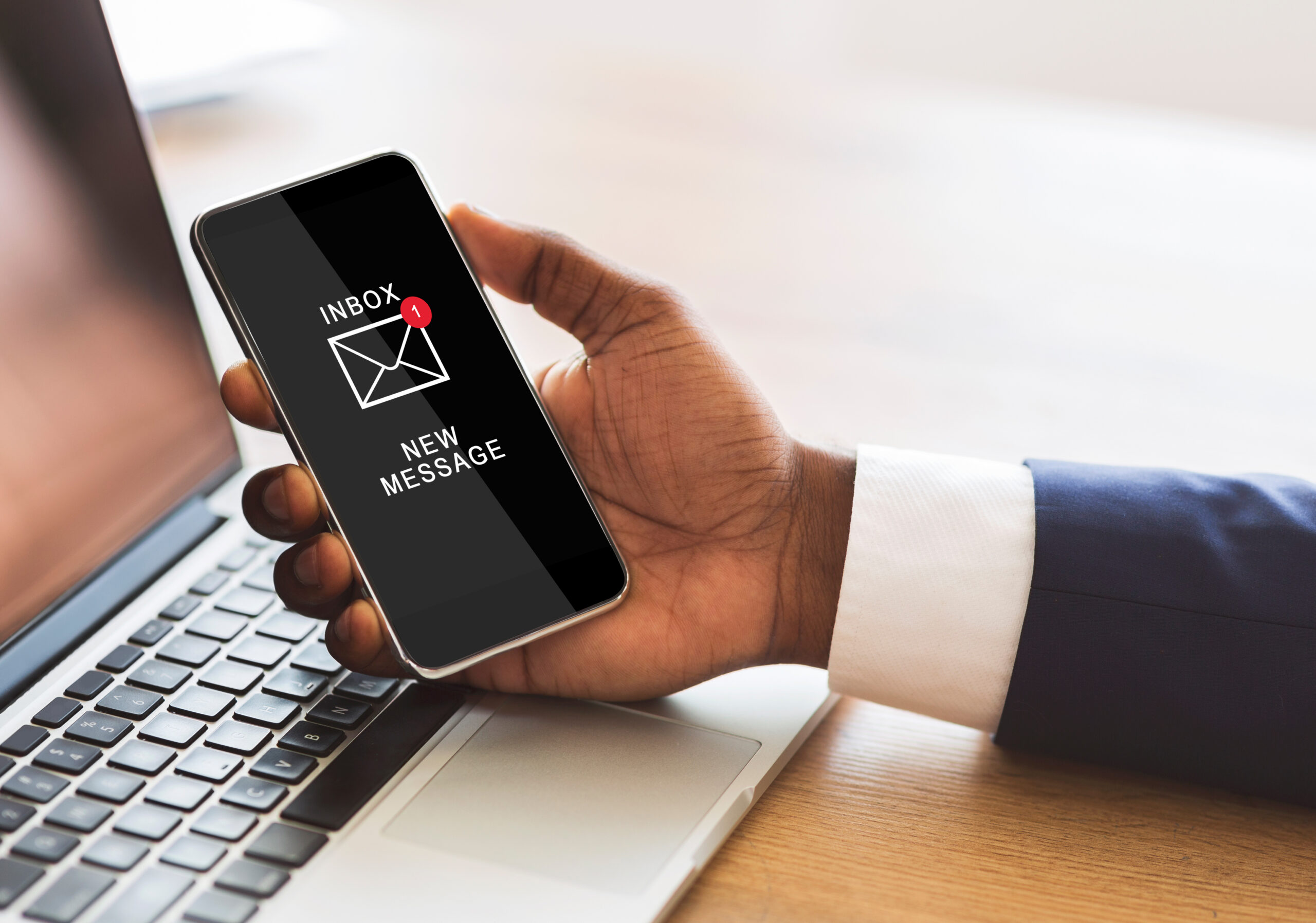 a hand holding a mobile phone showing a notification for a new email, next to a laptop