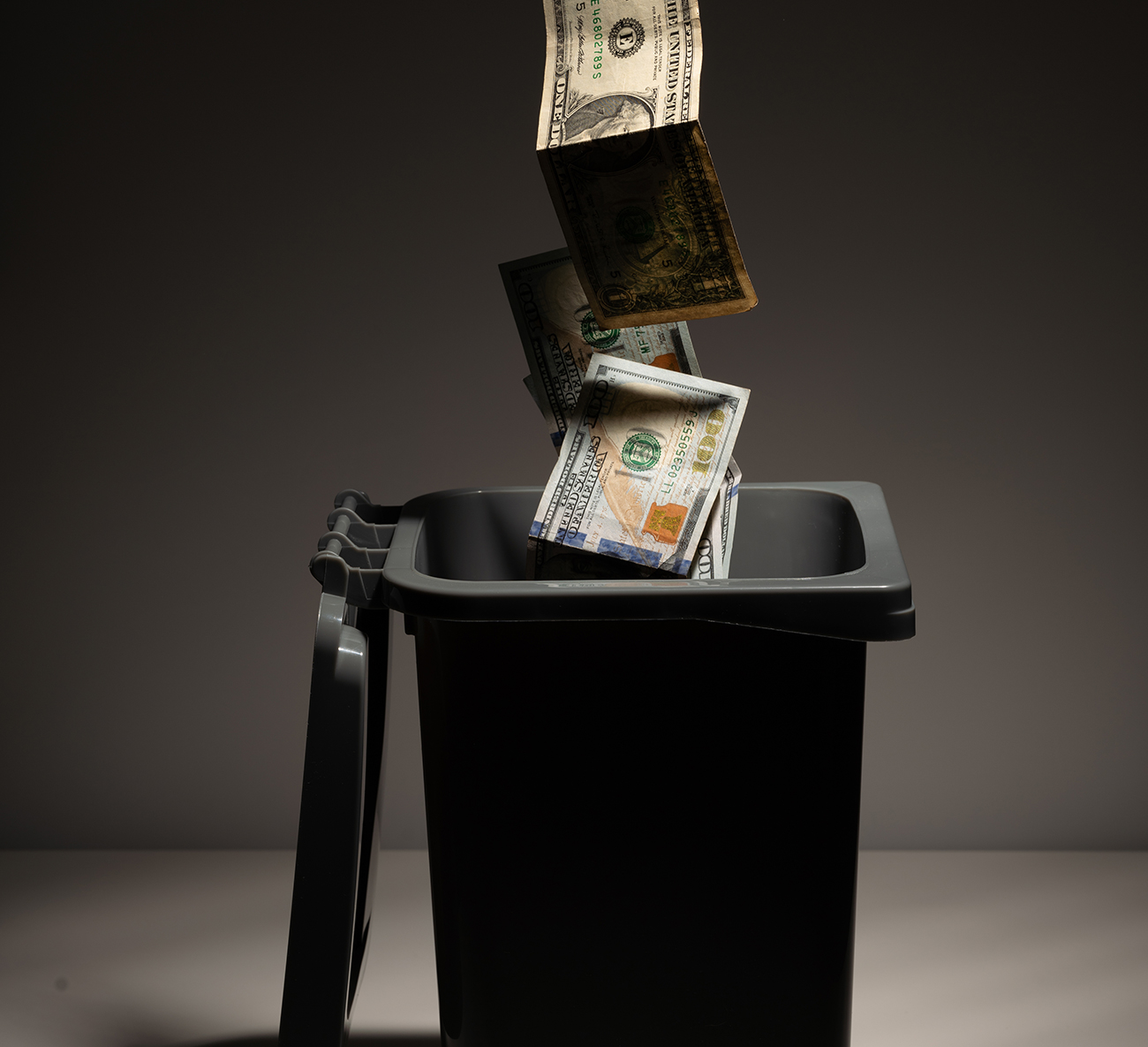 Dollar bills falling into a garbage bin.